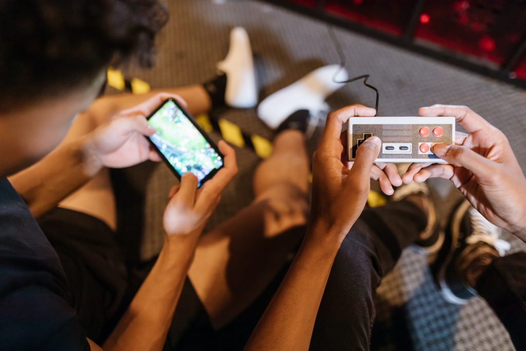two people sitting next to each other with one holding an old NES controller and the second holding a smartphone